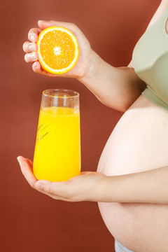 孕妇手上拿着一杯橙汁和半边橙子