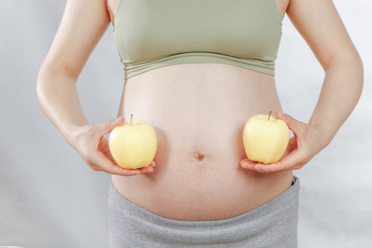 年轻孕妇手上拿着两个牛奶苹果