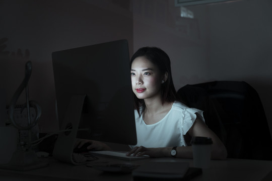 在办公室里对着电脑工作到午夜的亚洲女商人——超时工作的概念。