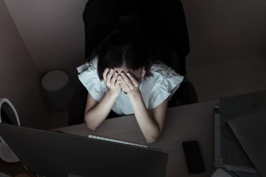 紧张的亚洲女商人在办公室对着电脑工作到午夜。不健康的状况。偏头痛和头痛。