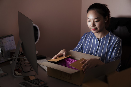 亚裔女性在房间里打开电脑前的送货箱-送货服务理念。
