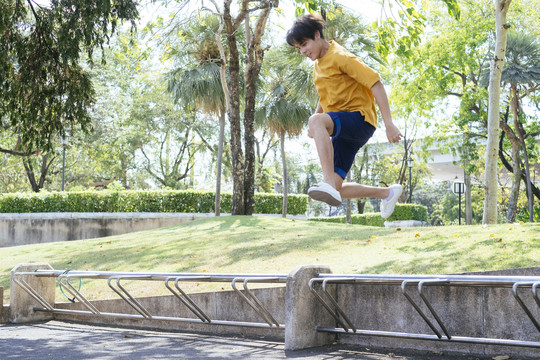 一个穿着黄色t恤和蓝色裤子的男孩在绿色公园里跳过停车场。