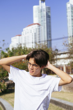 黑头发的家伙穿着白t恤，戴着眼镜站在田野里，背景是高楼大厦。