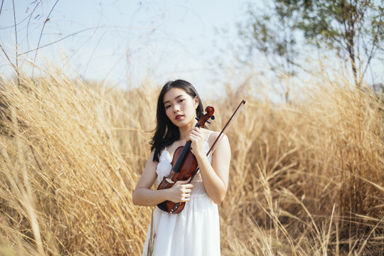 黑色长发小提琴手身穿白裙的女子手持小提琴站在草原上。