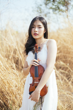 一位身着白裙的黑色卷发女子站在草原上拥抱小提琴。