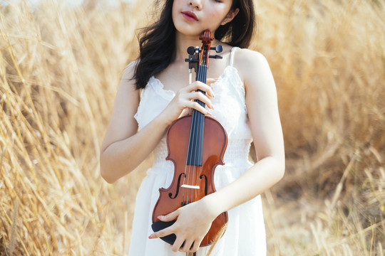 剪短的黑色卷曲长发女人抱着她心爱的小提琴在草原上闭着眼睛。