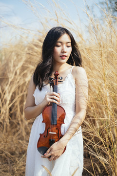 在风和日丽的草原上，一位身穿白裙的黑发女子在她面前拉着小提琴。