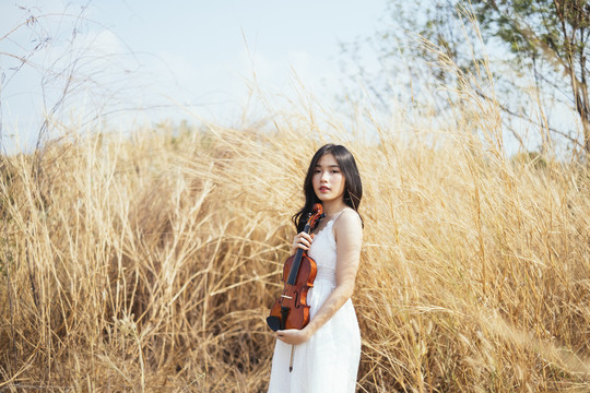 站在草原上，一个黑色长发女孩像抱着婴儿一样，手里拿着小提琴。