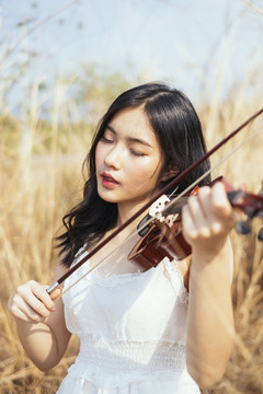风和日丽的草原上，黑发白衣女子拉小提琴。