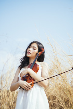 卷曲的长发白衣女子以草原和蓝天为背景，轻轻地抱着小提琴。