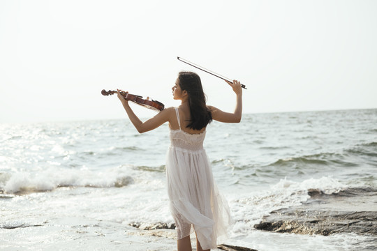 白衣女子在海浪中拉小提琴的后景。