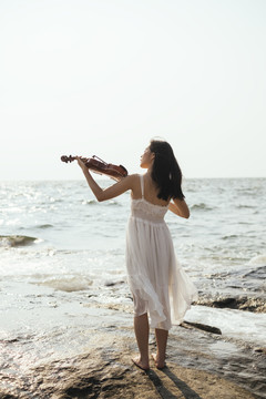 白衣女子在海上拉小提琴的背照，波浪，垂直。