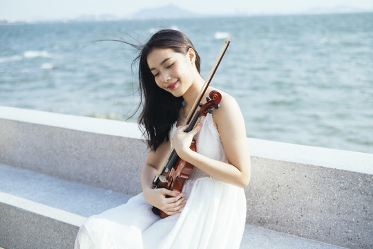 风和日丽，坐在大理石长凳上的白衣黑发美女抱着小提琴。