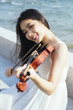 美丽的黑色长发白衣女子在大风天坐在大理石长凳上拉小提琴。