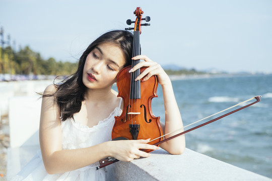 一位身穿白裙的黑发女子坐在大理石长凳上，把头靠在小提琴上。