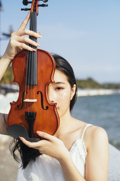 黑发白衣女子站在阳光下，把小提琴举到脸前。