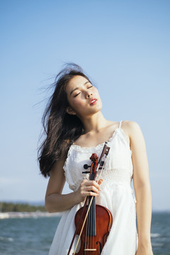 在刮风的日子里，美丽的长发白衣女子手持小提琴面对阳光。