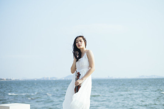 白衣美女站在海边，风吹着她的头发和衣服。