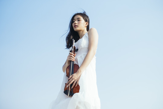 以天空为背景的黑色长发女人和她的小提琴的低角度拍摄。