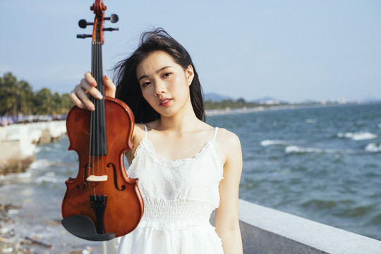 在风和日丽的海上，一位黑色长发女子向镜头展示小提琴。