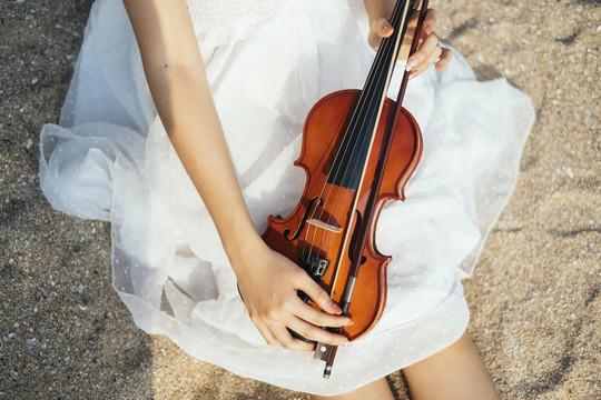 沙滩上白裙女人腿上的小提琴剪短图像。