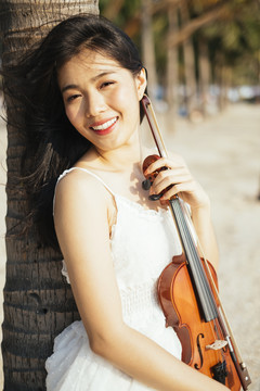 黑色长发女子倚在椰子树上，胸前放着小提琴。