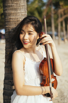 风大的日子里，一个黑发女人靠在椰子树上，胸前放着小提琴。