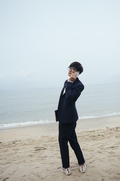 黑发黑衣人站在沙滩上，在模糊的天空下打电话。