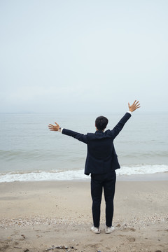 站在沙滩上的黑发黑衣人张开双臂捂着头，像是在迎接海风。