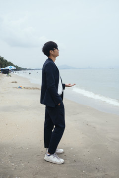 黑发黑衣人站在沙滩上伸手看海。