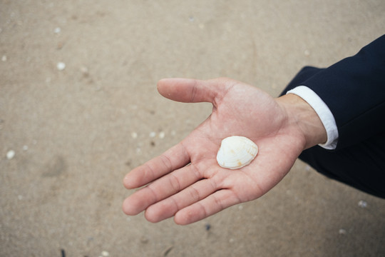 沙滩上男人手上白色贝壳的剪影。