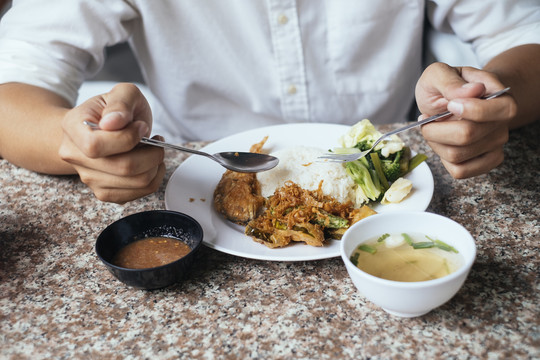 一张被剪下来的照片，照片上的食物放在白衬衫前面，一个男人在午餐时间拿着勺子和叉子，一顿饭。
