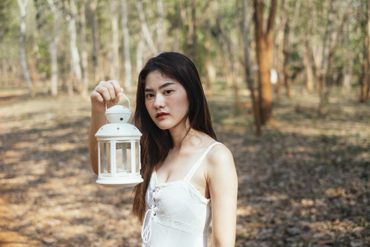 特写镜头：美丽的年轻女子穿着优雅的白色连衣裙，在森林里展示白油古董灯笼。