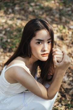 特写镜头中美丽的年轻女子穿着优雅的白色连衣裙，坐在森林里。