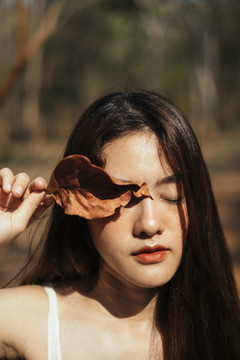 美丽的亚洲年轻女子穿着白色连衣裙，秋叶闭上眼睛的特写镜头。