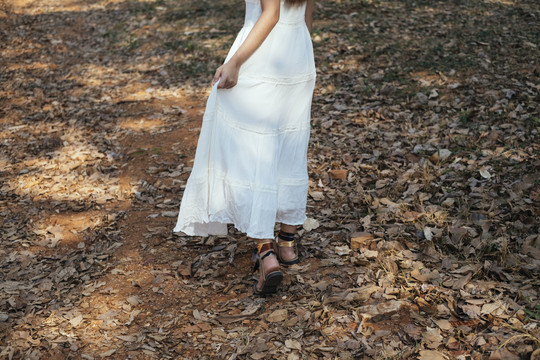 美丽的年轻女子穿着优雅的白裙独自行走在森林里。