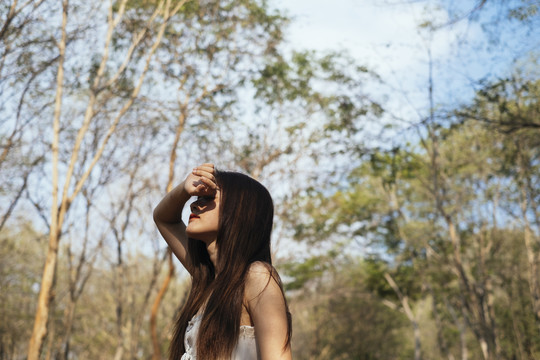 美丽的年轻女子穿着优雅的白色连衣裙，胳膊搭在脸上，站在森林里。
