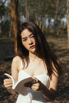 美丽的年轻女子穿着优雅的白裙在森林里看书的特写镜头。