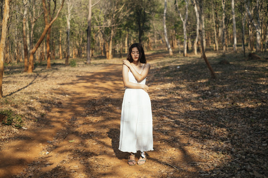 爱你自己的概念-美丽的年轻女子穿着优雅的白色礼服拥抱自己，独自站在森林里。