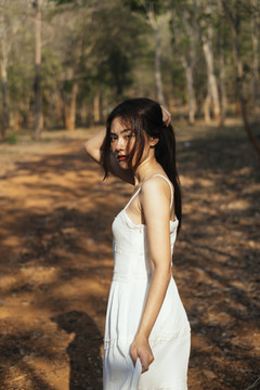 夕阳下，美丽的年轻女子穿着优雅的白裙在森林中的肖像。