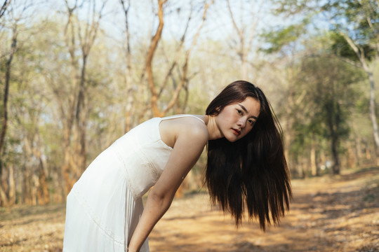 画中美丽的年轻女子身穿优雅的白色连衣裙，弯腰站在森林里。