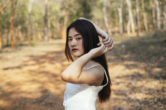 美丽的年轻女子穿着优雅的白色连衣裙在森林里摆姿势的肖像。