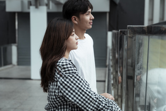 一对年轻夫妇站在玻璃路障旁的天桥上，看着城市。