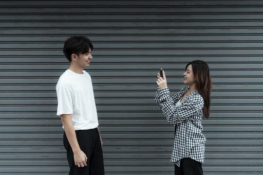 一个穿黑白格子花呢的女孩在百叶门前为她的男朋友拍照。