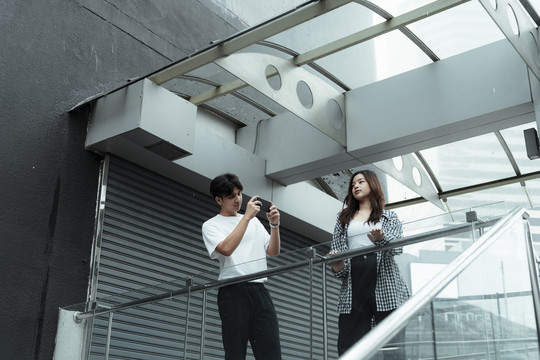 一个穿黑白衣服的家伙在玻璃路障给他的女朋友拍照。