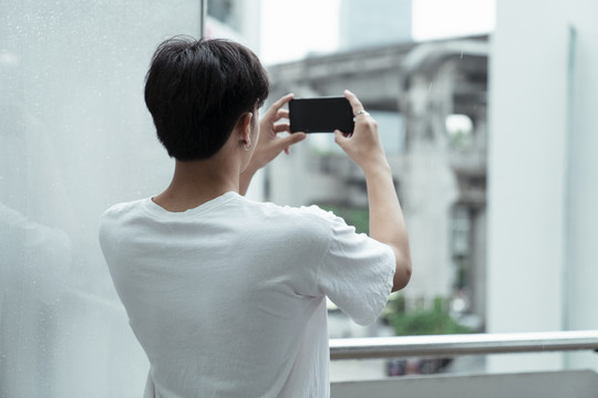 黑色头发，穿着白色t恤的家伙举着智能手机拍了一张城市的照片。