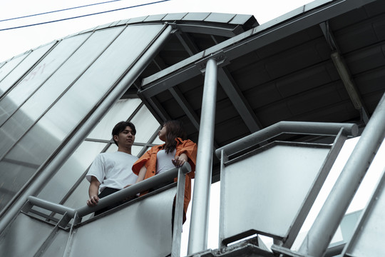 一对年轻夫妇站在天桥上，抓住扶手互相对视的低角度镜头。