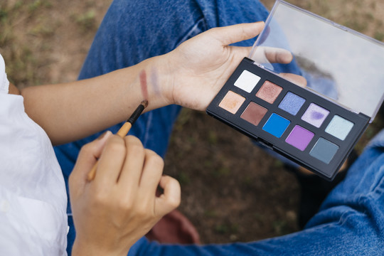 一个女孩的特写镜头用调色板上的化妆品给她的手臂涂颜色测试。