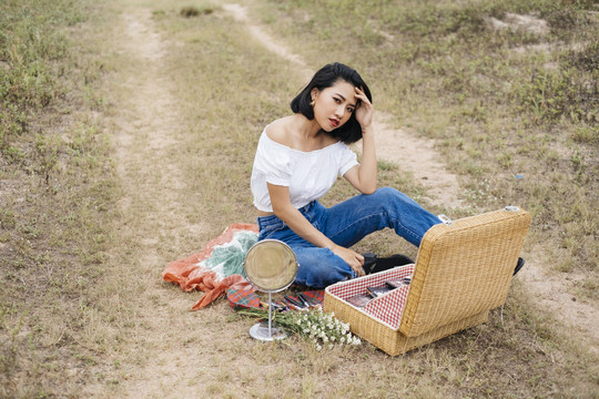 性感的亚洲女人正在野餐，独自坐在乡下的田野上，提着一个大篮子。