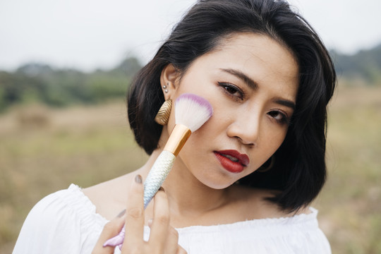性感的亚洲女人在乡村用刷子在脸上化妆。